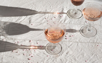 Rose wine in vintage glasses with blooming pink branches, flower petals, romantic mood, spring vibes. Eco linen background, natural spring light, romantic still life