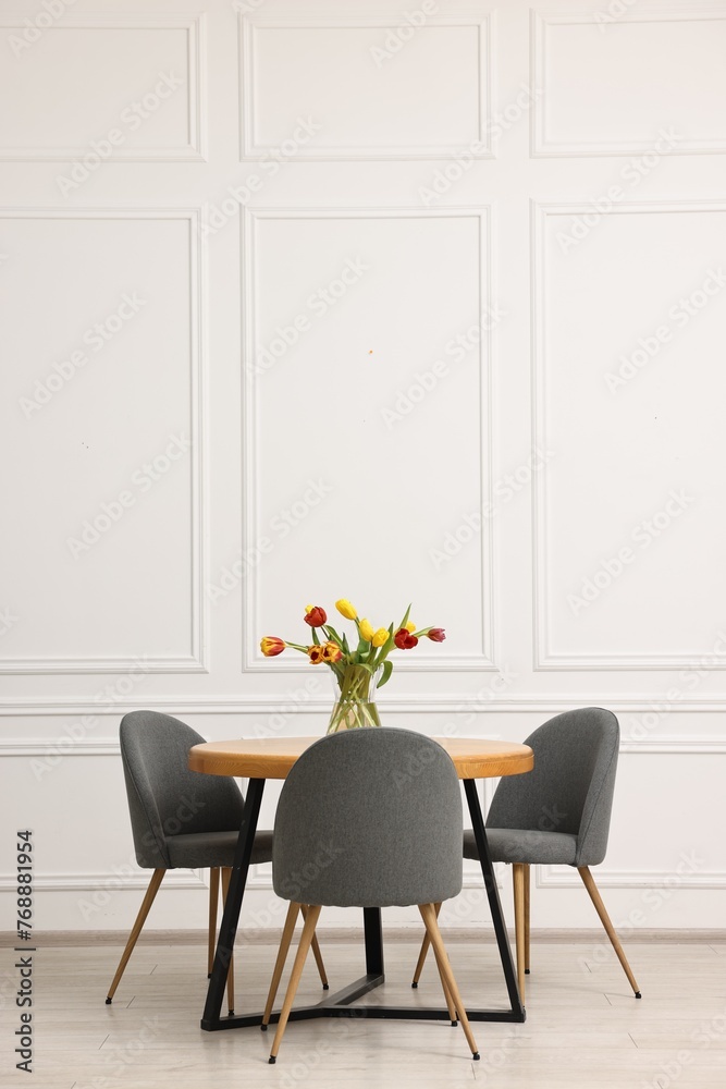 Wall mural Stylish dining room interior with comfortable furniture and beautiful tulips. Space for text