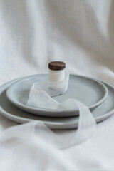 A composition of ceramic dishware in varying shades of muted gray, artistically arranged on a textured linen backdrop. A spindle with white thread, topped with a dark wooden cap.