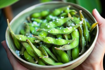 person holding a bowl of edamame beans with salt