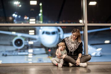 Riga, Latvia - October 19, 2019 - A woman and a toddler are sitting on the floor by an airport...