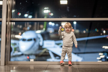 Riga, Latvia - October 19, 2019 - A joyful toddler in a gray outfit with red shoes stands by a...