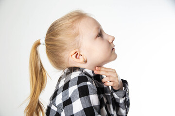 A blonde girl aged seven holds her sore throat with her hands. Sore throat and allergies in children. Inflammation of the lymph nodes, bacterium