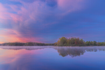 Foggy spring landscape at dawn of the shoreline of Whitford Lake with mirrored reflections in calm water, Fort Custer State Park, Michigan, USA