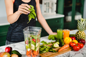 Young girl making green detox cocktail of fresh vegetables and fruits using blender in the kitchen....