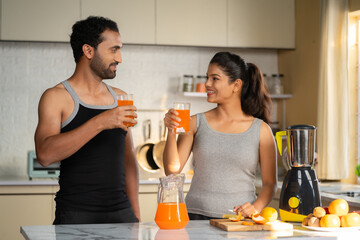 Joyful active healthy couples drinking nutritious orange juice after workout at kitchen - concept of healthy lifestyle, morning routine and relationship bonding