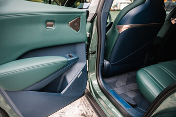 The back door of the car is open. Inside view of a car seat with green leather and golden design. Part luxury car detail. Interior of prestige modern electric car. Concept of future. Passenger door.