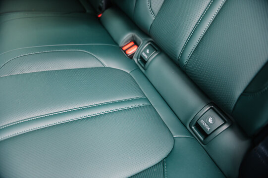 Installing ISOFIX baby and car seat for maximum safety. Part of green perforated leather car seat. Fastening child seat with isofix system. Luxury car inside. Interior of prestige modern electric car.