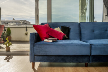 A blue velvet sofa next to a window that overlooks a terrace