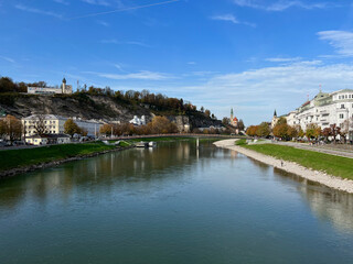 Obraz premium View of the Salzach River from the Staatsbrücke in Salzburg, Austria. The scenic river is flanked by historic buildings and picturesque landscapes.