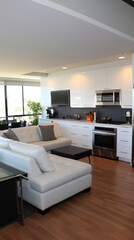 An open-concept living space with a white sectional sofa, hardwood floors, and a large kitchen with stainless steel appliances.