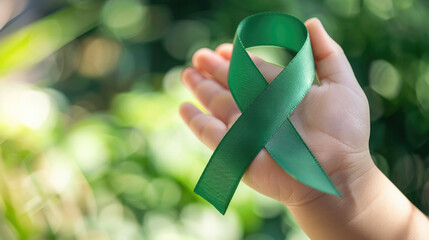 Mental health awareness week background - green ribbon in a baby hand with bokeh background