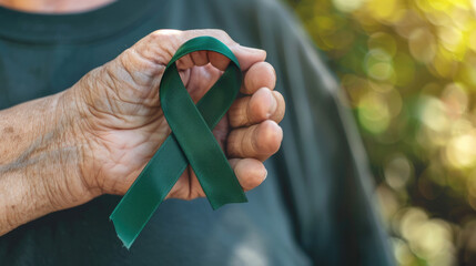 Mental health awareness week background - green ribbon in a elderly hand with bokeh background