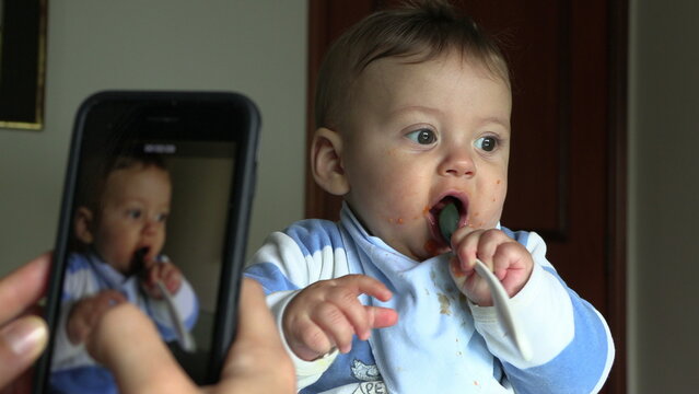 Parent taking photo of baby. Mother filming toddler son during meal