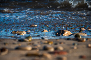 Selective focus on the sand and stones of a beach with the sea breaker in the background.