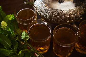 Close up of glasses with green tea with mint and silver teapot near fresh mint leaves. Moroccan...