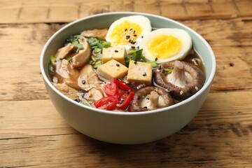 Bowl of delicious ramen on wooden table, closeup. Noodle soup