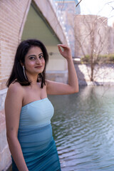 A woman in a blue and white dress stands in front of a bridge