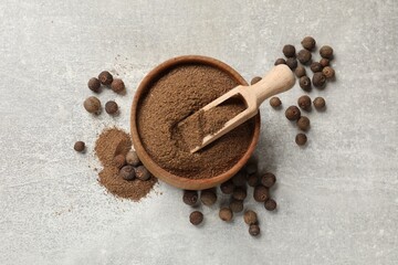 Ground allspice pepper in bowl, grains and scoop on grey table, flat lay