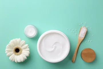 Keuken spatwand met foto Moisturizing cream in open jars, sea salt and gerbera flower on turquoise background, flat lay. Body care products © New Africa
