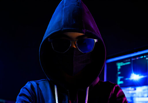 face of computer hacker wearing black hoodies and mask on dark background