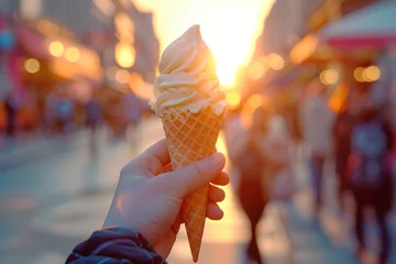 Foto auf Alu-Dibond A hand holding an ice cream cone on a blurred background of a street with people at sunset © Sergio