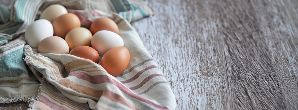 Fresh farm eggs on a linen cloth over a rustic wooden table. Farm and natural produce concept. Design for cookbook recipes, food blog headers with copy space, and organic product packaging.