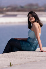 Fototapeta na wymiar A woman in a blue dress is sitting on a ledge by a body of water