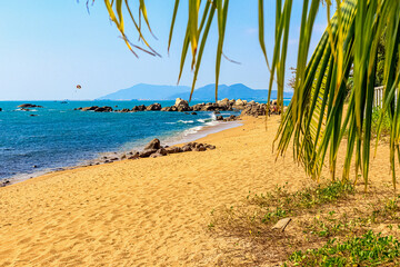 Fototapeta na wymiar View of the shore of the South China Sea with a sandy beach, large rocks and green palm. Sanya China
