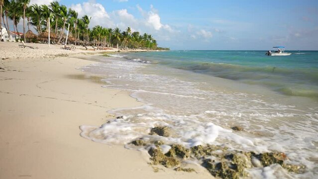 Close up of waves crashing on the rock in the sand. Bayahibe beach Playa Cadaques. Green palm trees in the background on the Caribbean sea shore. Vacations in Dominican Republic