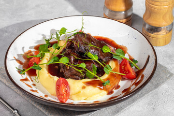 Mashed potatoes with beef in sweet and sour sauce, decorated with tomatoes and microgreens.
