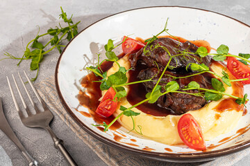 Mashed potatoes with beef in sweet and sour sauce, decorated with tomatoes and microgreens.