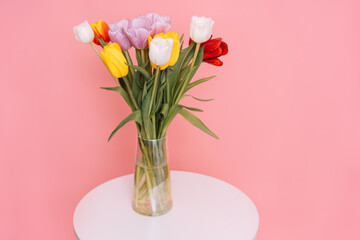 Bouquet of tulips in a glass vase on a white round table opposite a pink background.