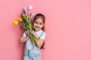 Child holding a bouquet of tulips in front of a pink background. - obrazy, fototapety, plakaty