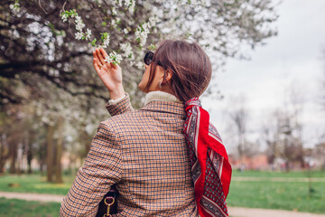 Back view of stylish woman wearing red hair scarf in spring park. Retro female fashion. Headscarf for bun hairstyle