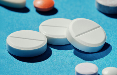 Pharmacy health care and drugs concept. Macro of three white tablets among different kinds of pills on blue background.
