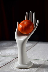 still life with a tangerine on a stand in the shape of a  hand made of white porcelain