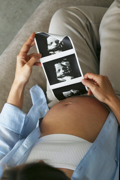 Pregnant woman at home on the couch admiring a fetus ultrasound photo. Background, copy space, close up.