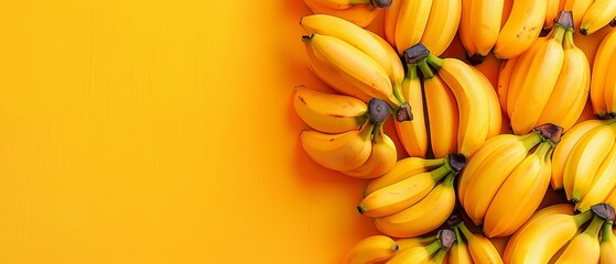   A group of ripe bananas are stacked on top of one another against a yellow backdrop with space for text - obrazy, fototapety, plakaty