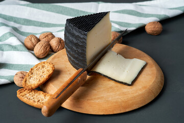 Cheese wedge on wooden board with sliced pieces and nuts