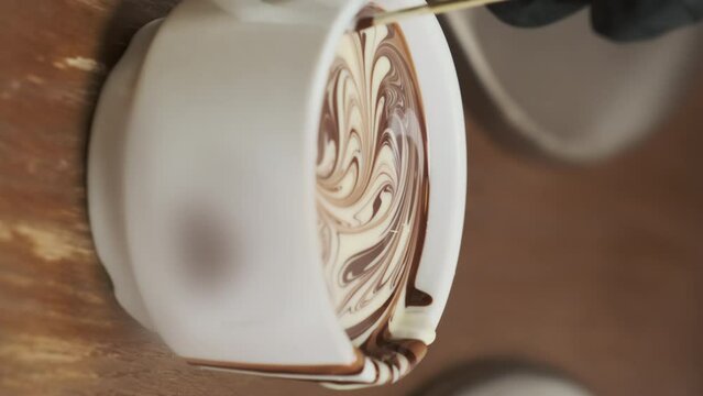 Barista skillfully creates chocolate pictures in cup closeup. Chef in gloves enhances both visual and gustatory appeal of beverage