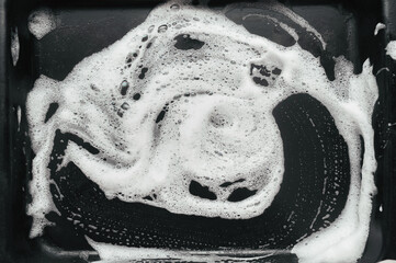 White foam and soap on dark background. Abstract pattern. The concept of washing oily pan or black car.