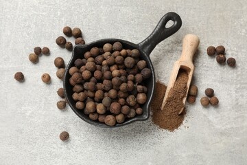 Ground allspice pepper, grains and scoop on grey table, flat lay
