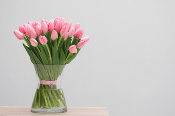 Bouquet of beautiful pink tulips in vase on wooden table against grey background, space for text