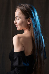 Classic studio portrait of a young brunette dressed in a black top, who is sitting on a chair against a black background.