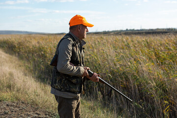 Mature man hunter with gun while walking on field.