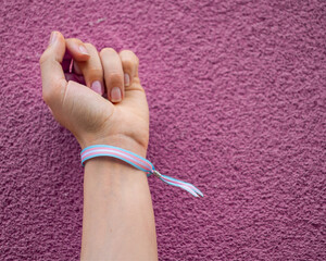 Close-up of a woman closed fist with transgender bracelet over violet pink background. Copy space