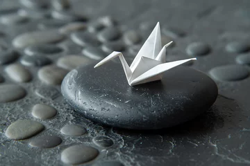 Fotobehang A single origami crane, perfectly folded from crisp white paper, resting on a smooth black stone © GraphicXpert11