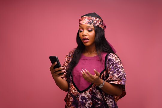 An African woman surprised and reacting to a message or notification from her smartphone.  Wearing an Ankara with headtie