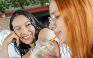 mujeres jóvenes latinas compartiendo una café en una tarde juntas y cuentan historias una de ellas le sonríe y mira con admiración  - obrazy, fototapety, plakaty